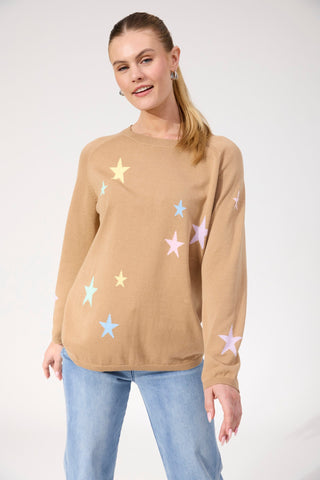 Woman wearing a tan knit sweatshirt with pastel star patterns and light blue jeans.