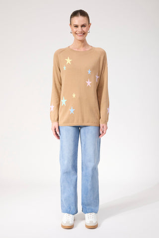 Woman wearing a tan long sleeve sweatshirt with pastel star patterns and light blue jeans.