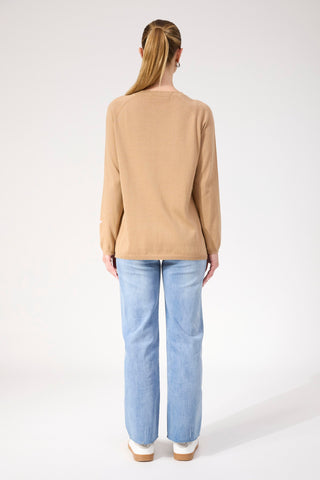 Woman wearing a tan long sleeve sweatshirt and light blue straight leg denim jeans.