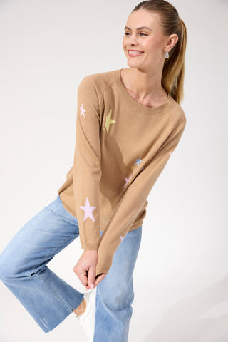 Woman wearing a tan star-patterned sweatshirt and light blue flared denim jeans.