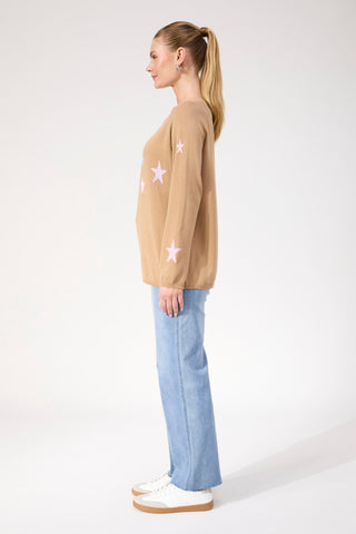 Woman wearing a tan star-patterned sweatshirt and light blue wide-leg jeans.