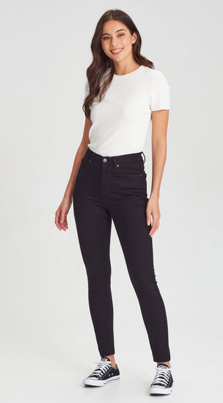 Woman wearing a white short-sleeve t-shirt and black slim-fit skinny jeans with black sneakers.
