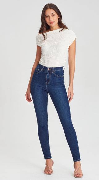 Woman wearing a white textured short sleeve top and dark blue skinny denim jeans.