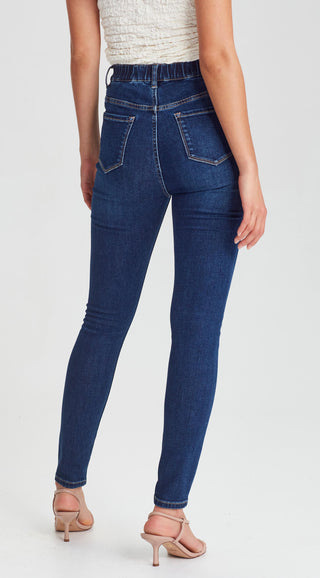 Woman wearing dark blue high-waisted skinny jeans with an elasticated waistband and nude heels.