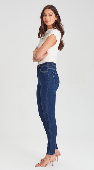 Woman wearing a white textured sleeveless top and dark blue skinny jeans with nude heels.