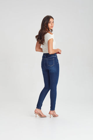 Woman wearing a white textured top and slim-fit dark blue denim jeans with high heels.
