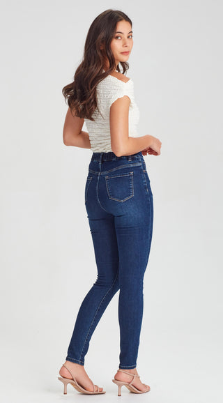 Woman wearing a white textured sleeveless top and dark blue skinny denim jeans.