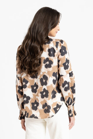 Back view of a woman wearing a tan, black and white leopard print blouse and white pants