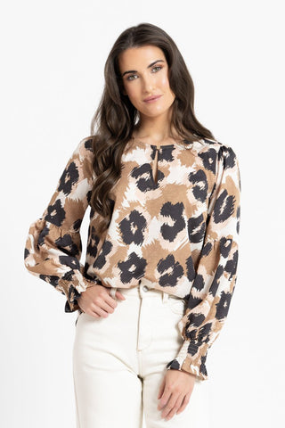Woman wearing a brown and black leopard print blouse with puff sleeves and white jeans.