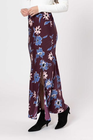 Woman wearing a floral print maxi skirt in burgundy with blue and pink flowers.