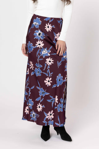 Woman wearing a long floral print maxi skirt in burgundy with blue and pink flowers.
