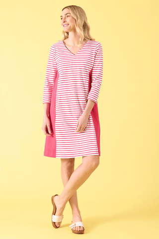 Woman wearing a pink and white striped v-neck dress with side panels and white sandals.
