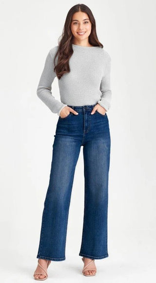 Woman wearing a grey long sleeve knit sweater and blue wide leg denim jeans.