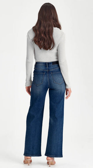 Woman wearing a grey long sleeve ribbed top and blue wide leg denim jeans.
