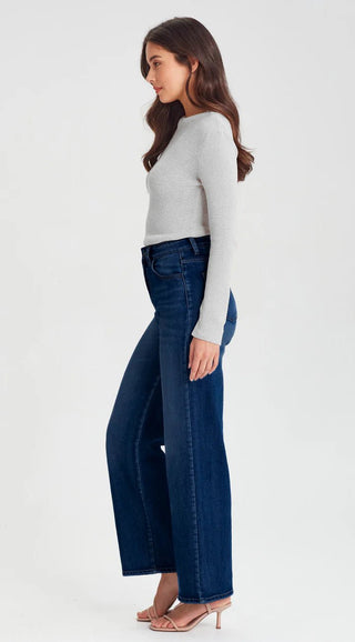Woman wearing a grey long sleeve knit top and dark blue wide leg denim jeans.