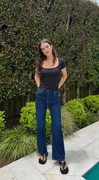 Woman wearing a black scoop neck t-shirt and blue flare denim jeans standing in a garden.