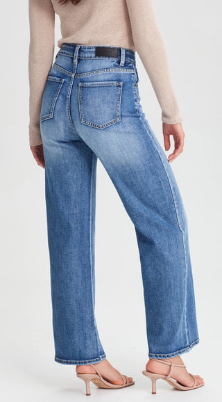 Woman wearing high-waisted blue straight-leg denim jeans and a beige knit sweater.