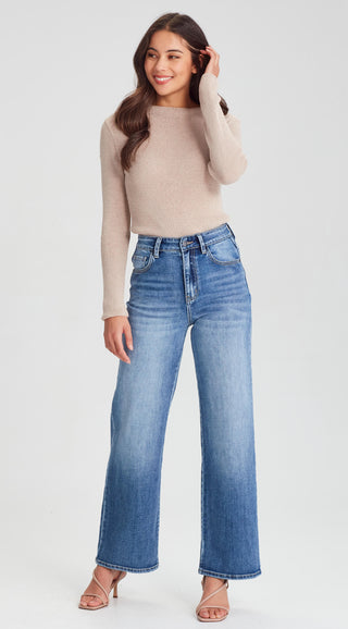 Woman wearing a beige ribbed long sleeve sweater and blue wide leg denim jeans.
