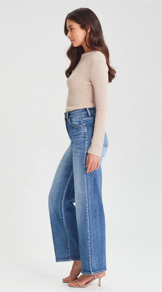 Woman wearing a beige long sleeve knit top and blue wide leg denim jeans.