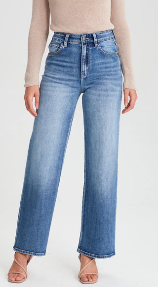 Woman wearing high-waisted blue wide leg denim jeans and a beige knit sweater.