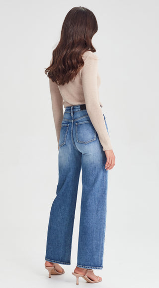 Woman wearing high-waisted blue wide-leg jeans and a beige long-sleeve knit top.