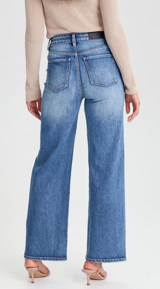 Woman wearing high-waisted wide leg blue denim jeans and a beige long sleeve top.