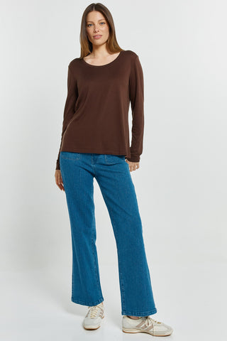 Woman wearing a brown long sleeve top and blue flare jeans with white sneakers.