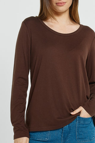 Woman wearing a brown long-sleeve crew neck top and blue jeans.