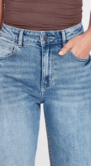 Woman wearing light wash blue denim jeans and a brown ribbed top.