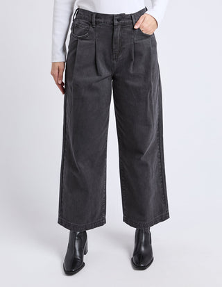 Woman wearing wide-leg charcoal grey pleated trousers and black heeled boots.