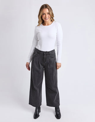 Woman wearing a white long sleeve t-shirt and grey wide leg pleated trousers.